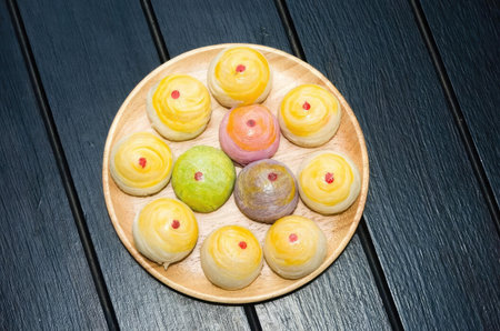 A plate of assorted mochi with various fillings and colors, arranged on a wooden table with a dark background.