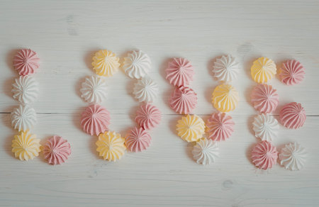 The image features colorful pompoms arranged to form a word on a white wooden background. The pompoms are pink, yellow, and white.