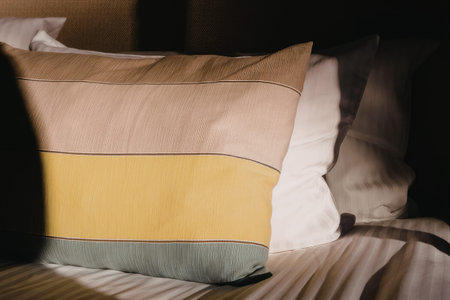 Soft pillows rest on a comfortable bed with striped bedsheet, creating a cozy bedroom atmosphere illuminated by natural light.