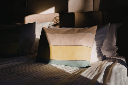 Softly lit bedroom features a comfortable bed with a yellow, blue and brown striped pillow, creating a cozy atmosphere with modern and inviting decor.