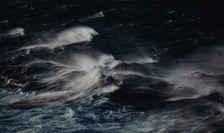 Powerful ocean waves crash with white foam against dark blue water creating a dramatic seascape scene with turbulent and frothy ocean spray.