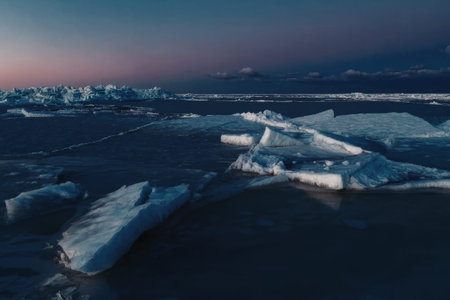 Large fragmented blocks of bright white ice float on deep blue water under a vibrant purple and blue twilight sky creating a stark natural contrast.