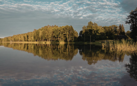 a calm lake reflecting the surrounding trees and sky on a partly cloudy day