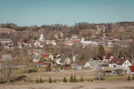 a small town with many houses and trees on a hill, with a field in the foreground and a clear blue sky