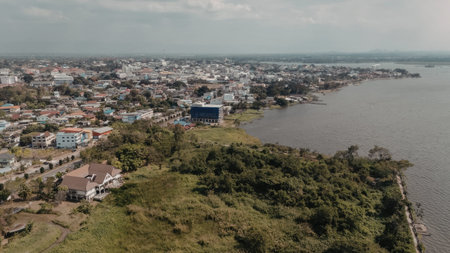 a highly pixelated aerial view of a cityscape situated next to a large body of water with a mountain range in the distance under a cloudy sky