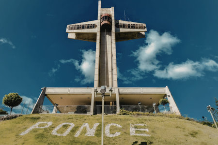 a large cross on a hill with a building in the background and a blue sky with clouds