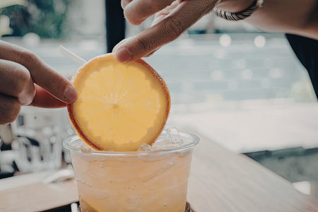 a close up of a hand holding a lemon slice above a cup of iced drink, possibly in an outdoor summer setting