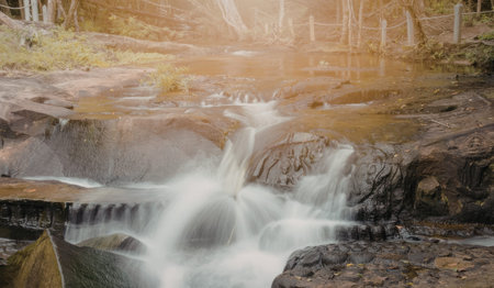 a small waterfall on a rocky stream with greenery and a brown background
