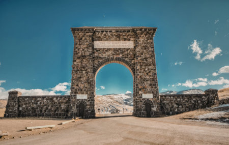 a large stone archway with a sign on top stands in a desert landscape with a blue sky and white clouds in the background