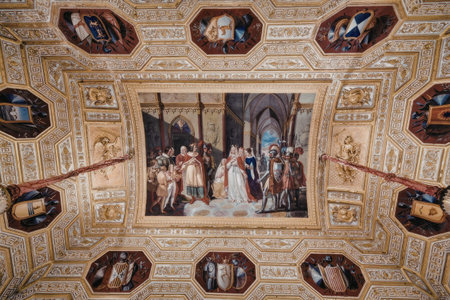 a highly ornamental ceiling featuring a central rectangular painting surrounded by multiple octagonal portraits each set within an intricate gold frame adorned with various designs and patterns