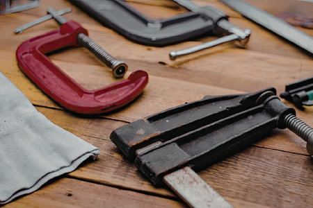 A selection of clamps and tools laid out on a wooden workbench, including a red clamp and a black clamp.