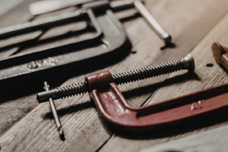 A close-up view of clamp tools on a wooden workbench, featuring a red clamp in the foreground and black clamps in the background.