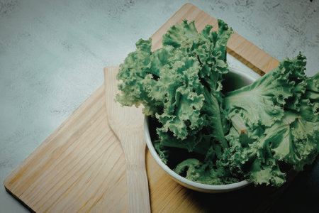 A bowl of fresh green kale leaves on a wooden cutting board