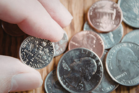 A hand holding a coin among a pile of various coins on a wooden surface