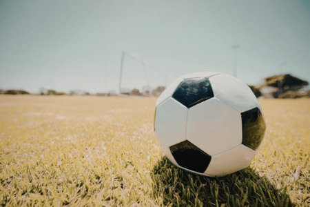 a soccer ball sitting on a green field with a clear blue sky and a large metal structure in the background