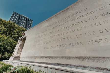 a large stone monument with writing on it, standing in front of a building and trees, with a blue sky in the background