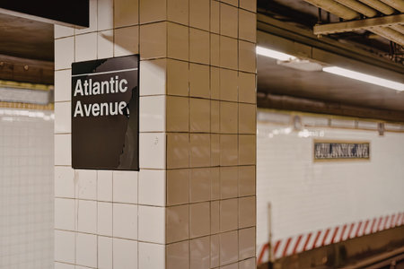 a black sign with white text on a white tiled wall reading atlantic avenue