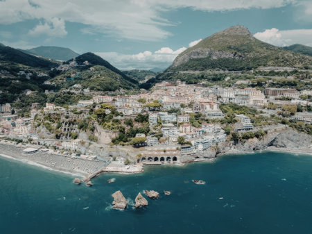 an aerial view of a coastal town with buildings and trees on a mountainous coastline, with a beach and rocks in the water
