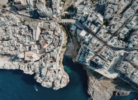 An aerial view of a coastal town with white buildings situated on a cliffside, featuring a body of water and a bridge connecting two landmasses.