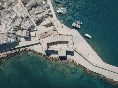 an aerial view of a small coastal town with a pier extending into the water, several boats are moored in the harbor, and buildings line the shore