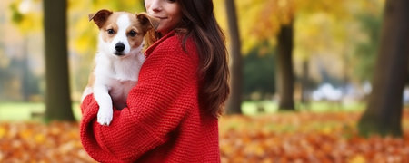 Attractive young woman with long brunette hair, wearing oversized red sweater in park her Jack Russell Terrier puppy, yellow leaves on the ground. Generative AIの素材