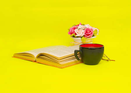 Cup of coffee with book isolated on yellow background