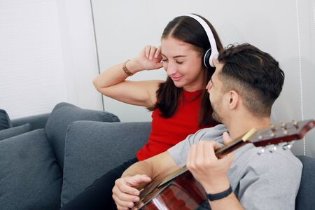 Smiling Caucasian Couple sitting and relaxing on sofa. Young woman listening to music by Headphones...
