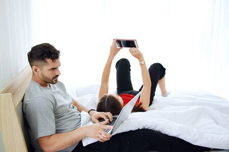 Smiling Caucasian Couple love playing games and working online for business with laptop in social media technology in bedroom. Work from home and family lifestyle on holiday Concept.の写真素材