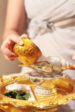 Woman hand hoding Gold cup for Pour water in conch shell on glod tray in tradition Thai wedding ceremonyの写真素材