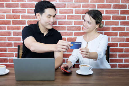 Smiling young business couple loves Asian man and caucasian woman holding credit card for online...