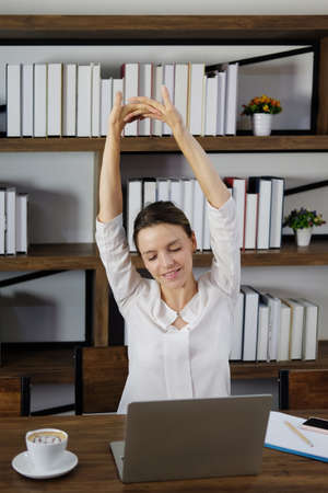 Smiling and lazy Caucasian woman stretch herself after working with laptop and dringking a cup hot coffee at workplace in cafe. Lifestyle of businesswoman and technology concept.の写真素材