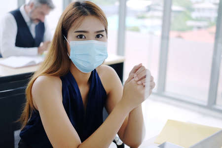 Young Asian businesswoman wearing mask preventing for Covid 19 virus and working in internationnal office. Social distance and new normal lifestyle conceptの写真素材