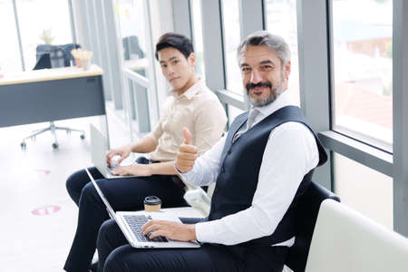 Smiling Senior Caucasian businessman Thumbs up and working with laptop in workspace at office. He...
