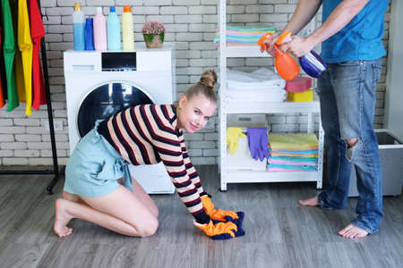Smiling Young Caucasian couple love husband and wife mopping wooden floor with sponges for housework...