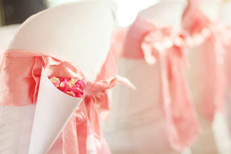 Beautiful Pink Rose petals Flowers with pink ribbon decoration on chairs in wedding event hall.の写真素材