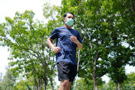Asian young man is wearing face mask for prevent Covid19 virus and running in the garden. Healthcare and exercise Conceptの写真素材
