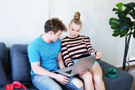 Smiling Young Caucasian couple love relaxing with laptop online for community in social media for shopping in website in living room. Technology for Married family lifestyle on holiday Concept.の写真素材