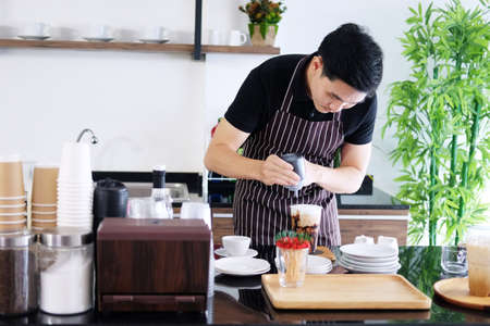 Asian barista young man pouring fresh Chocolate art in a plastic glass of Cappuccino iced coffee for according to order at counter bar in the morning at modern cafe and coffee shop.の写真素材