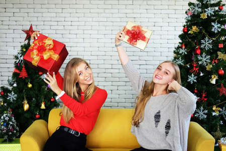 Smiling Caucasian teenage sister is showing big red gift boxes in Christmas party. Lifstyle on holiday and birthday concept.の写真素材