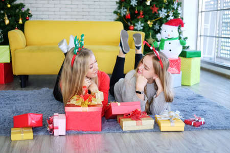 Smiling Caucasian Teenage couple girl laying on carpet and funny in Christmas party and decoration colorful Gift boxes and Lighting on pine tree with snowman in living room. Lovely lesbian on holiday.の写真素材