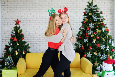 Smiling Caucasian Teenage couple girl hugging in Christmas party and decoration with yellow sofa, colorful Gift boxes and Light up the pine tree with snowman in living room. Lovely lesbian on holiday.の写真素材