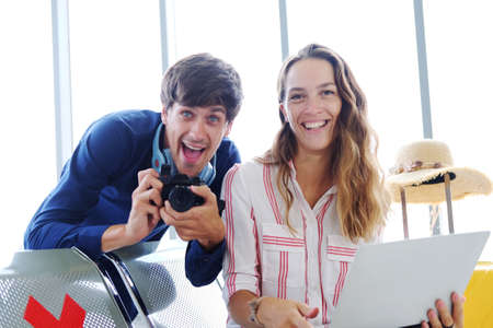 Smiling Young Caucasian traveler couple love is relaxing with camera and laptop for online social media together in the airport. Honeymoon trip on vacation concept.の写真素材