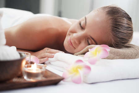 Smiling Caucasian woman in white  bath towel lie down and relaxing on bed preparing for massage therapy at alternative medicine healing spa Center in Thailandの写真素材