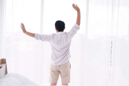 Asian man is Stretching lazily after waking up in bedroom.の写真素材