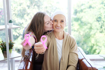 Caucasian daughter kiss Elderly mother in white headscarf is smiling and holding Awareness pink ribbon of common cancer is symbol of various campaign activities for patients with breast cancer.の写真素材