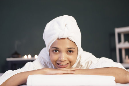 Smiling Asian woman in white headscarf and bath towel lie down on bed preparing for massage therapy at alternative medicine healing spa Center in Thailandの写真素材