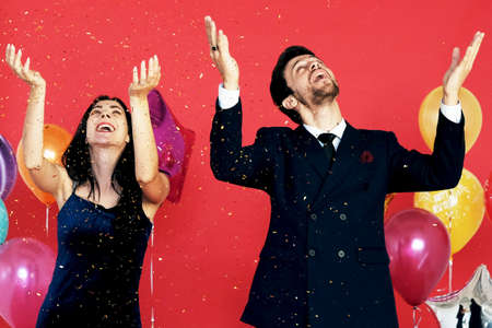 Couple love romantic Smile and dancing in Chrismas party, birthday time and celebration of New year eve and decoration with colorful ballons and  gold glitter sprinkle on red backgroundの写真素材