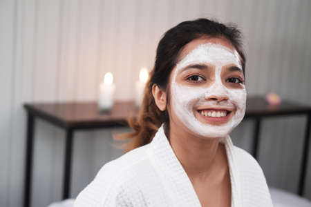Smiling young Asian woman is relaxing with facial masks for skine care on white bed together. Beauty salon and lifestyle Concept.の写真素材