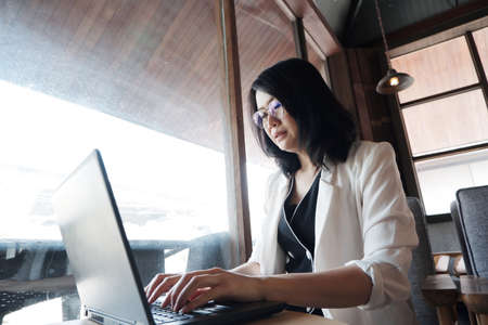 Asian woman is wearing glass online working or shopping with laptop in office. She is typing and searching information on internet. Businesswoman work with technology concept.の写真素材