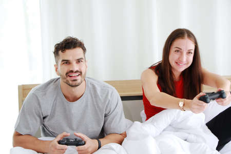 Smiling young Caucasian lover Couple hand holding joysticks and playing game play station together...